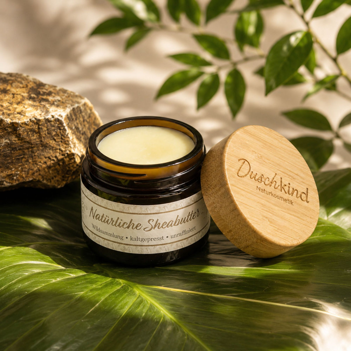 Duschkind Naturlig Sheabutter i åbent glas med bambuslåg på tropisk blad med natursten