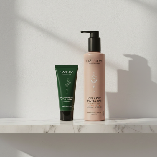 MÁDARA Hydra Soft Body Lotion og Deep Comfort Hand Cream stående på en elegant hvid marmorhylde mod en lys, minimalistisk væg med blødt lysindfald.